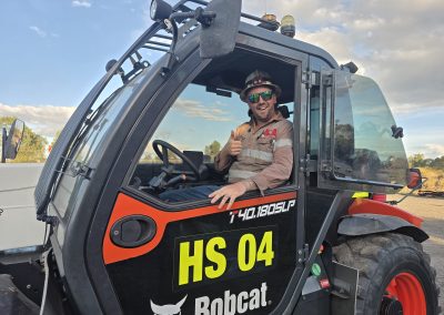 A man seated in the driver's seat of a tractor, focused on operating the vehicle in a rural setting.